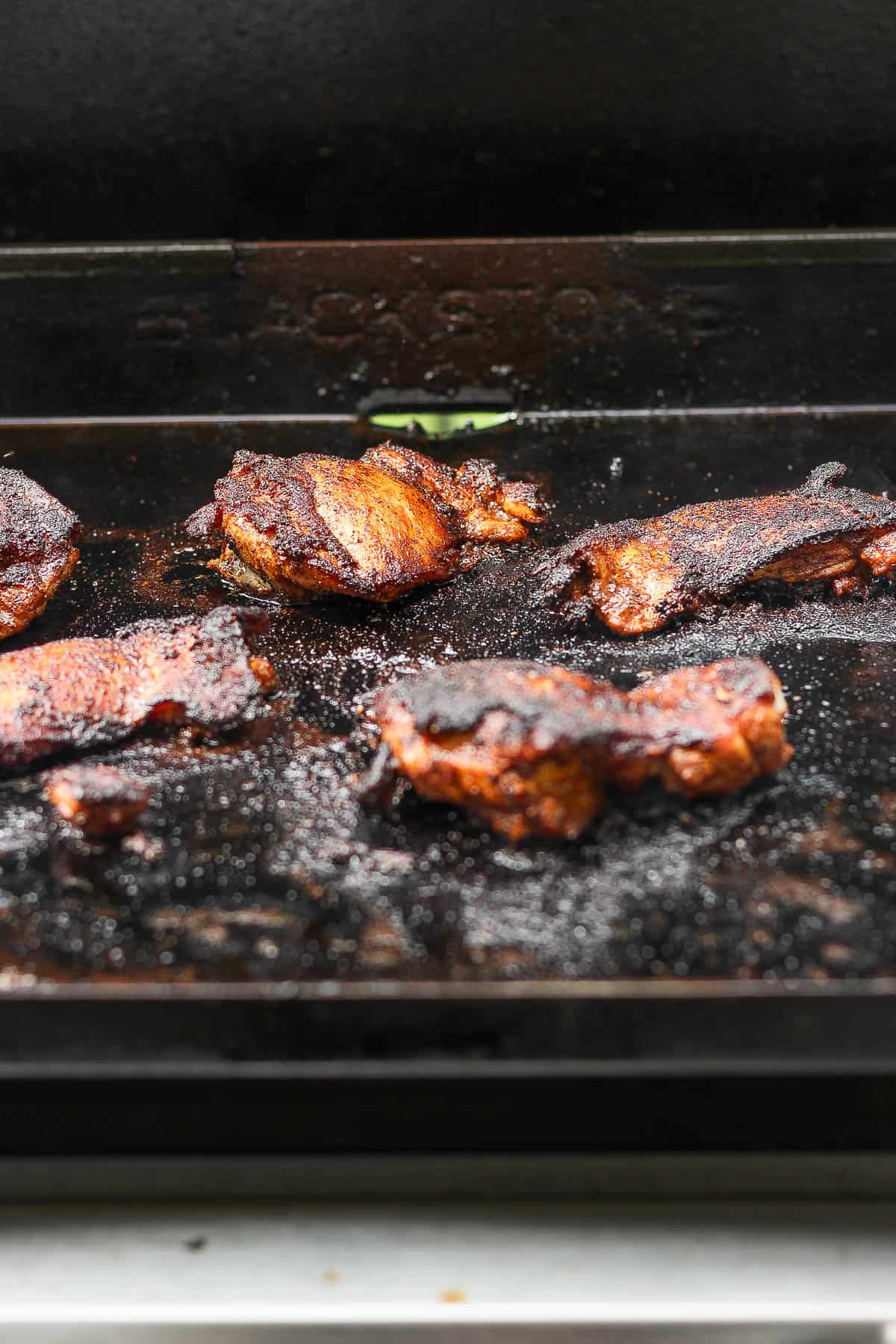 The seasoned chicken thighs cooking on the griddle.