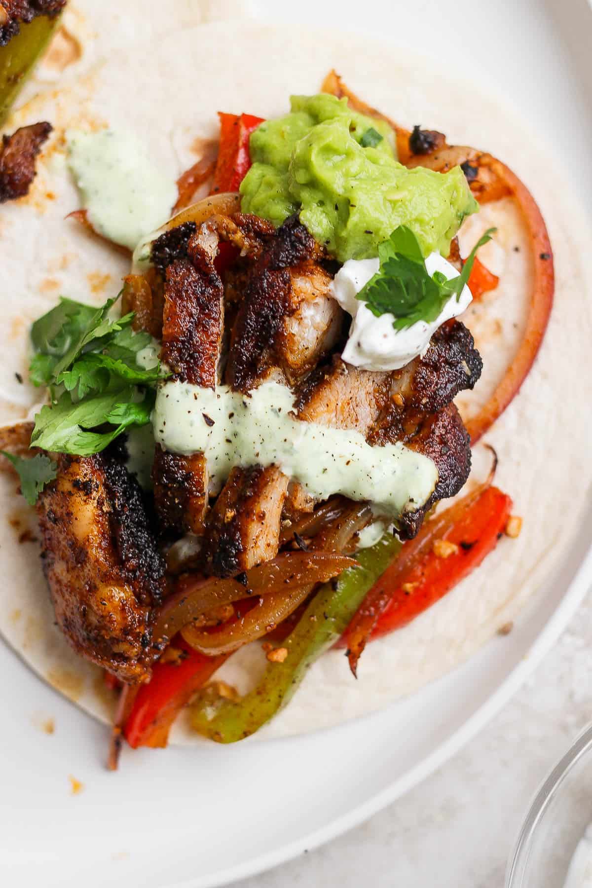 An assembled chicken fajita on a tortilla and with toppings on top.