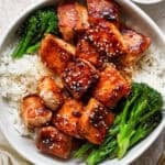 Top down shot of a bowl of rice with broccolini on the sides with cooked salmon bites in the middle with sesame seeds on top.