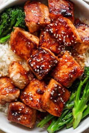 Top down shot of a bowl of rice with broccolini on the sides with cooked salmon bites in the middle with sesame seeds on top.