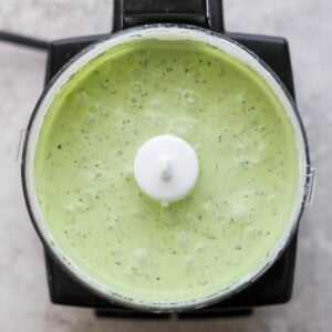 Top down shot of a small food processor full of blended green cilantro yogurt sauce.