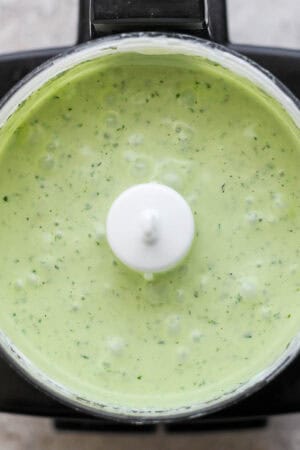 Top down shot of a small food processor full of blended green cilantro yogurt sauce.
