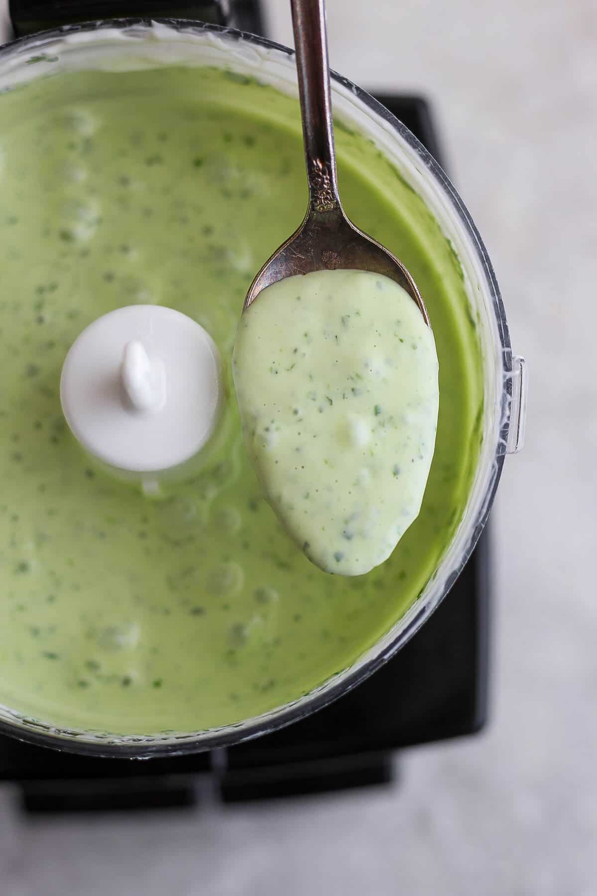 A spoon scooping some of the sauce out of the food processor.