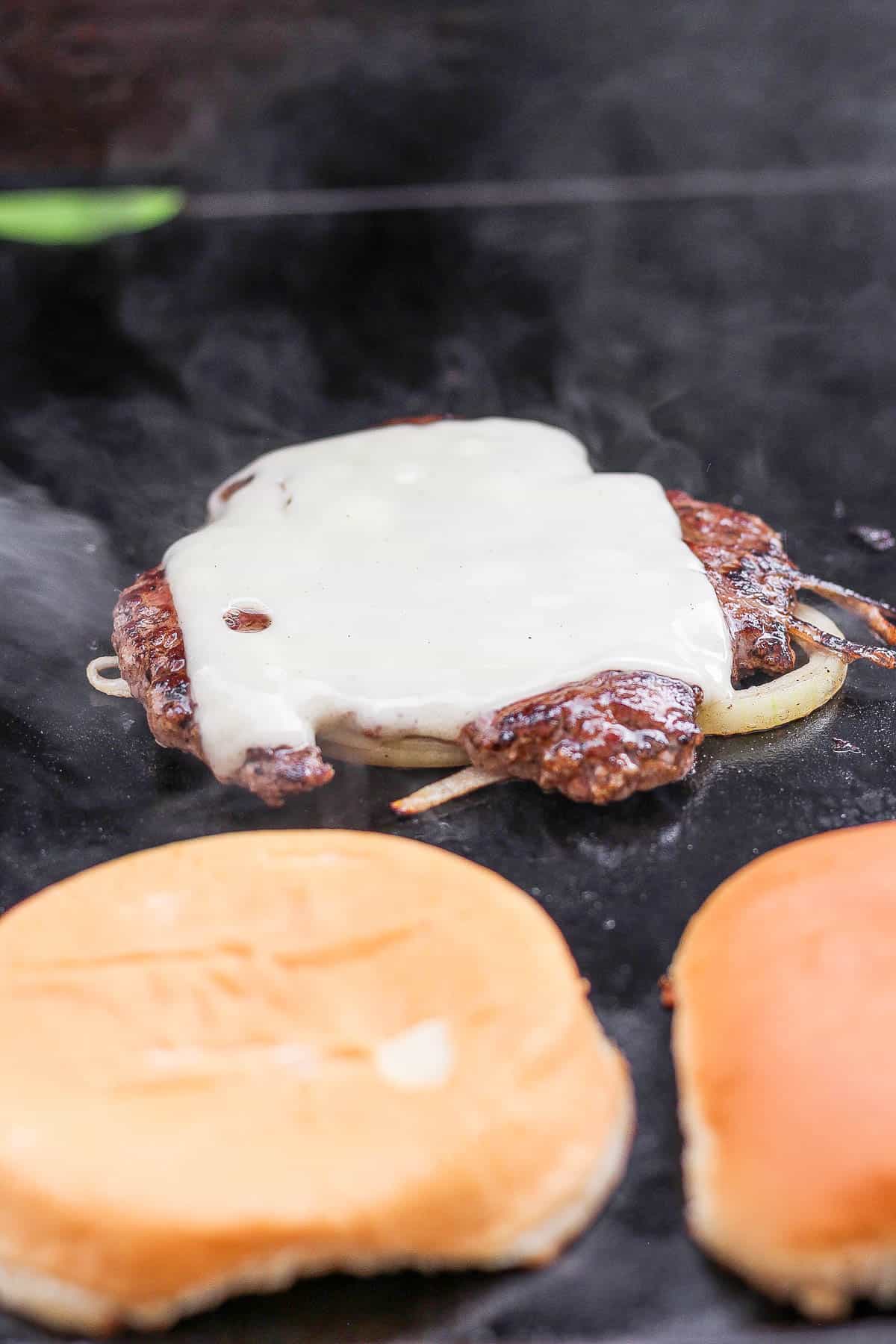 A smashed burger patty with cheese on top and buns next to it.