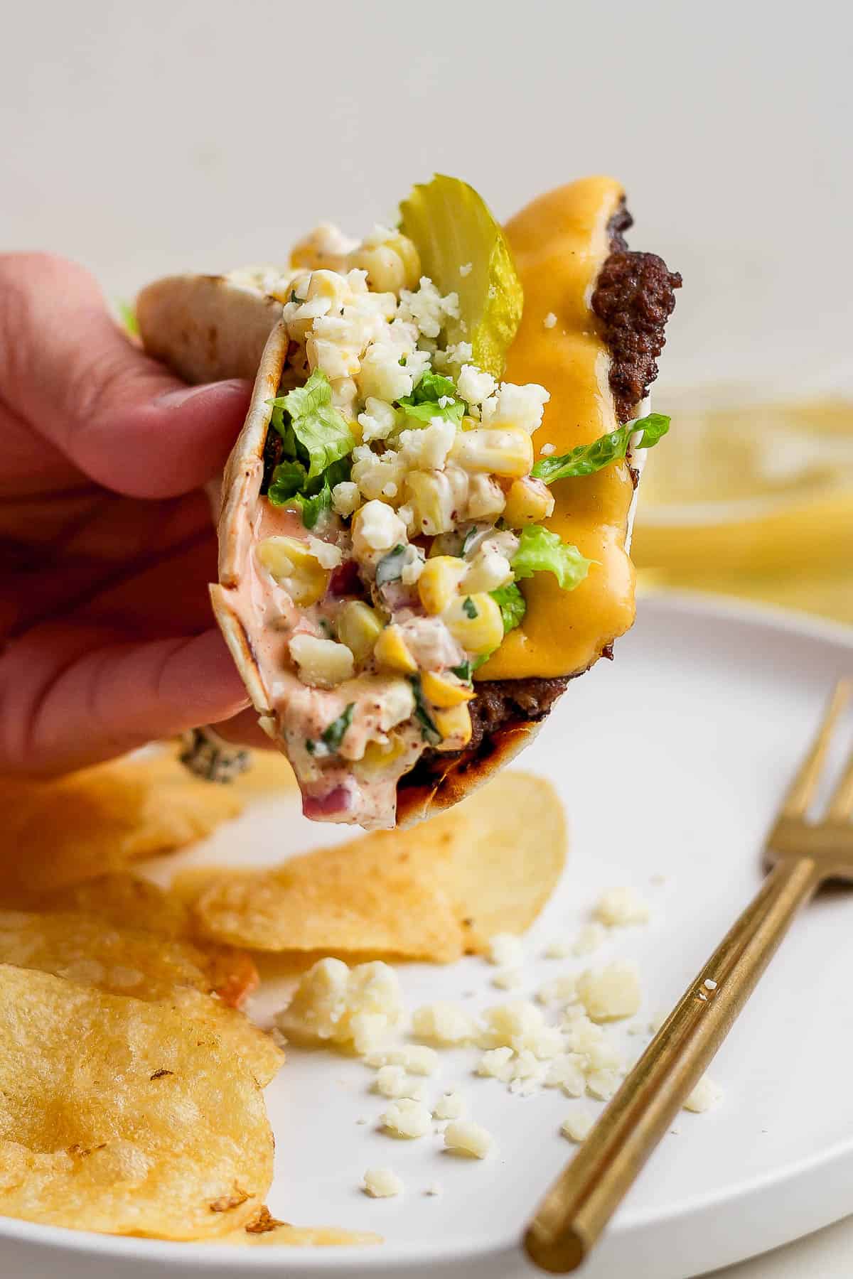 A hand holding the Mexican street corn smash burger taco over a plate.