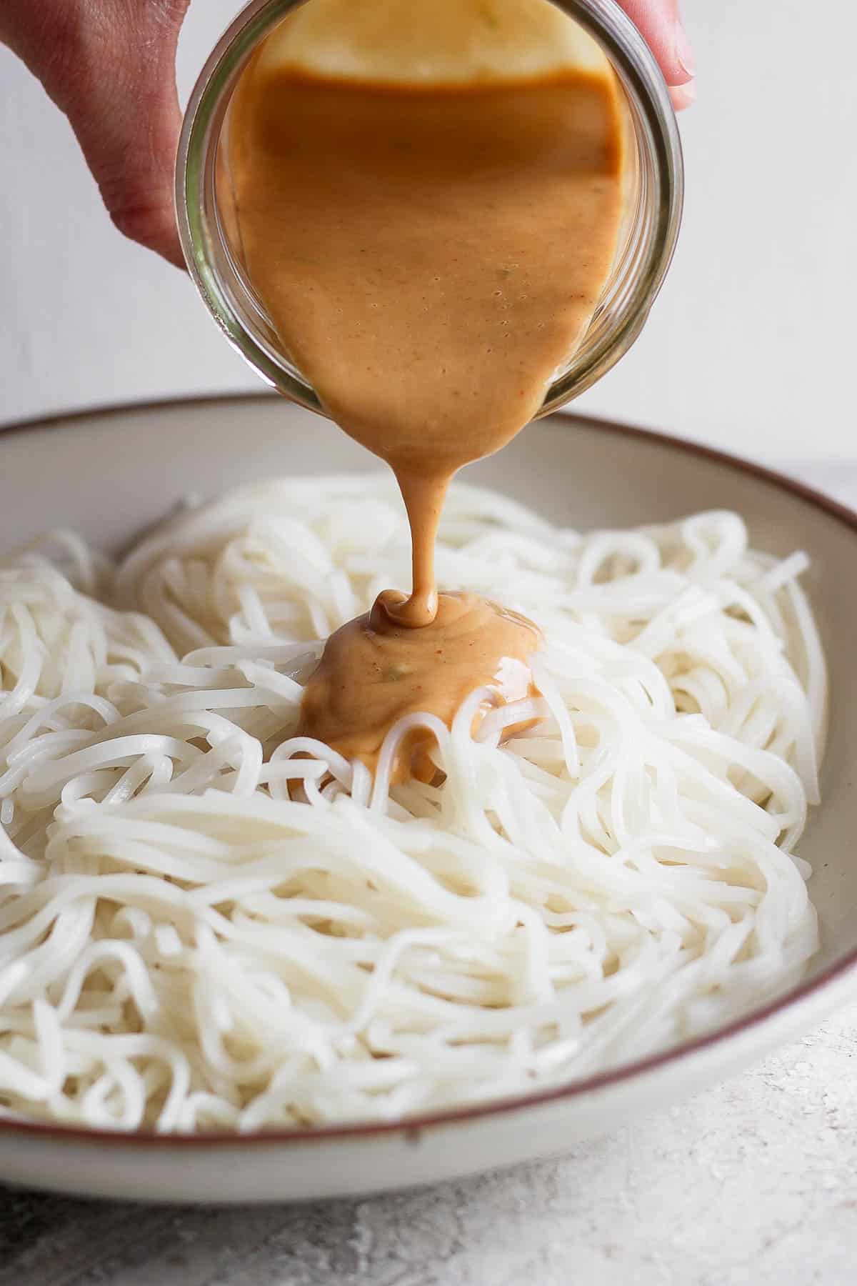 Peanut sauce being poured over rice noodles.