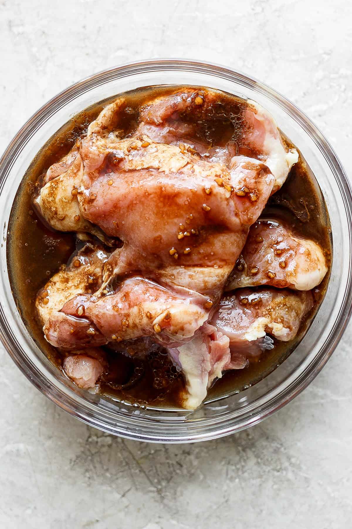 Chicken thighs marinating in the balsamic chicken marinade in a glass bowl.