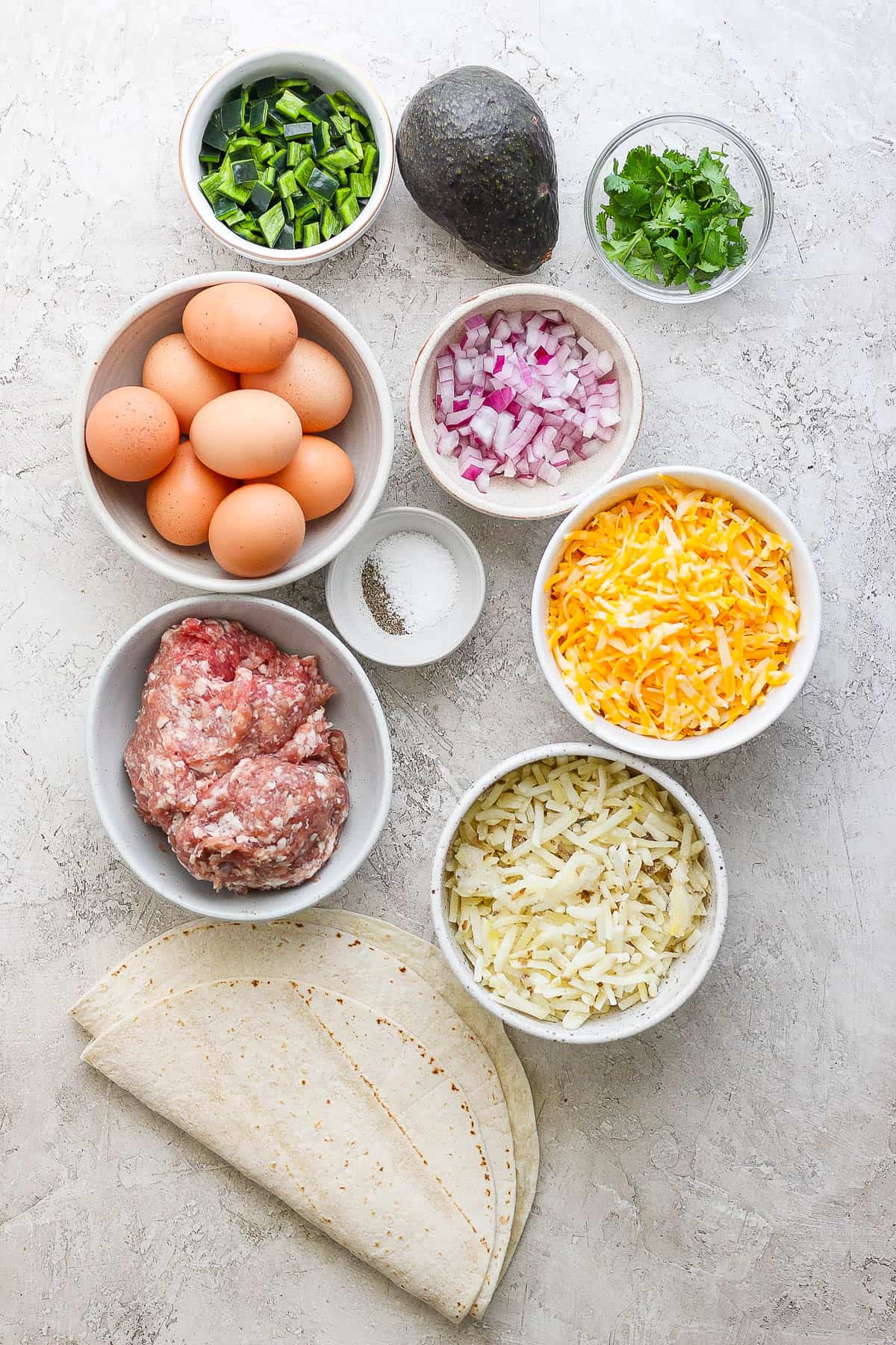 Ingredients for breakfast burritos in separate bowls.