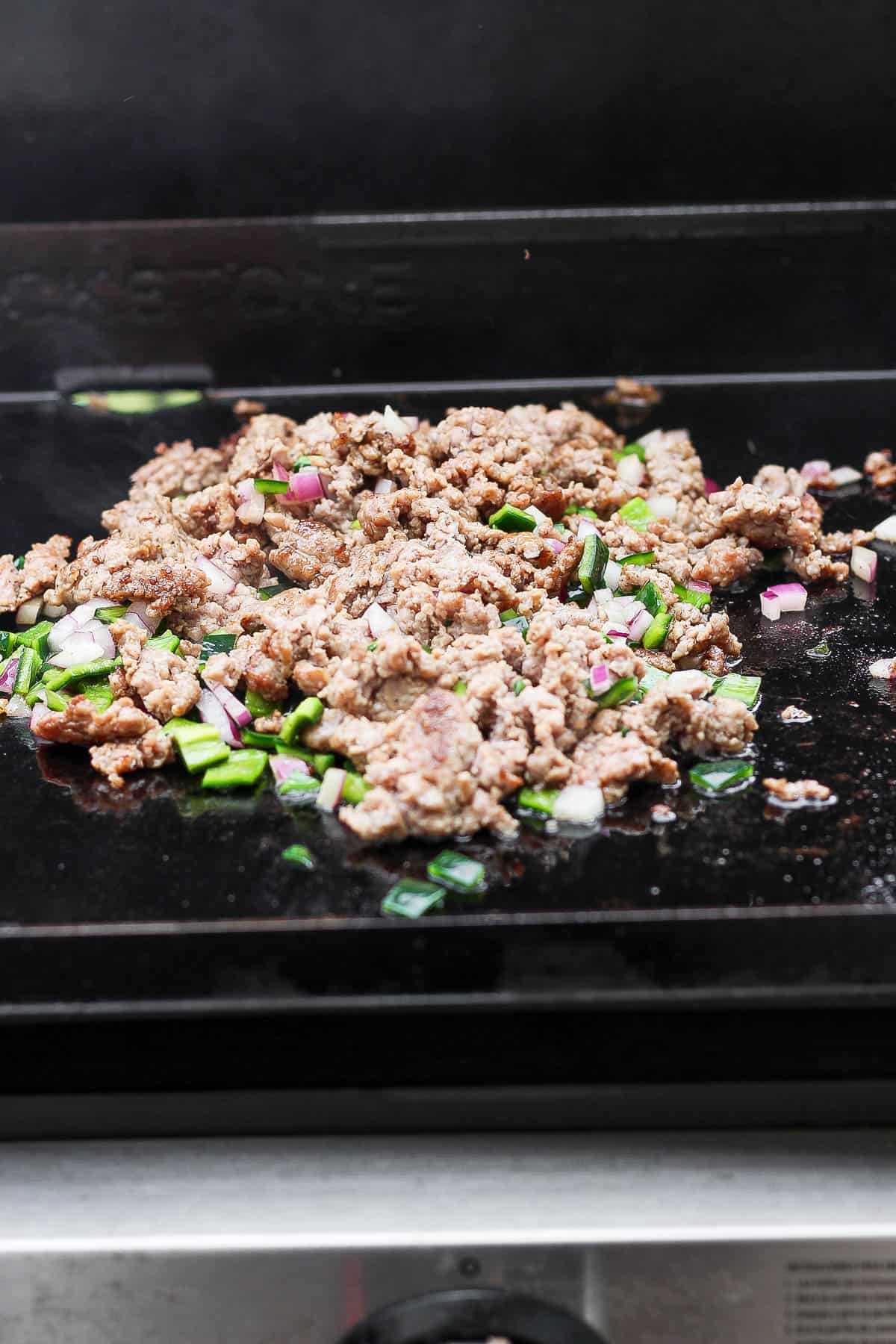 Breakfast sausage, onion, and pepper cooking on the griddle.