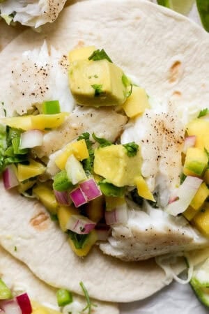 Close up shot of a flat street taco tortilla topped with a grilled fish taco with avocado mango salsa.