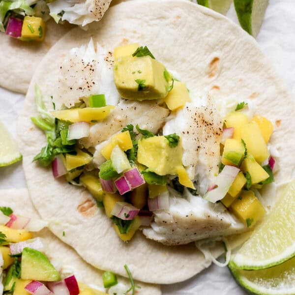 Close up shot of a flat street taco tortilla topped with a grilled fish taco with avocado mango salsa.