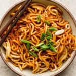 Bowl of Hibachi Noodles in a bowl with two chopsticks on the side and some sliced green onions on top.