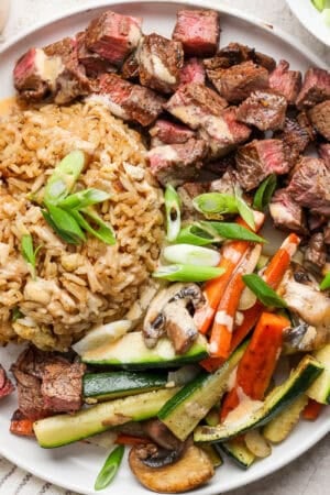 Plate of hibachi steak, fried rice and hibachi vegetables on a plate with Yum Yum Sauce drizzled on top.