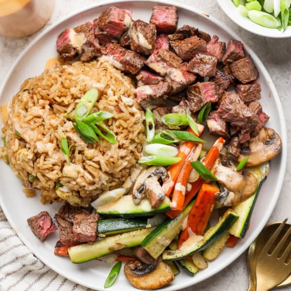 Plate of hibachi steak, fried rice and hibachi vegetables on a plate with Yum Yum Sauce drizzled on top.