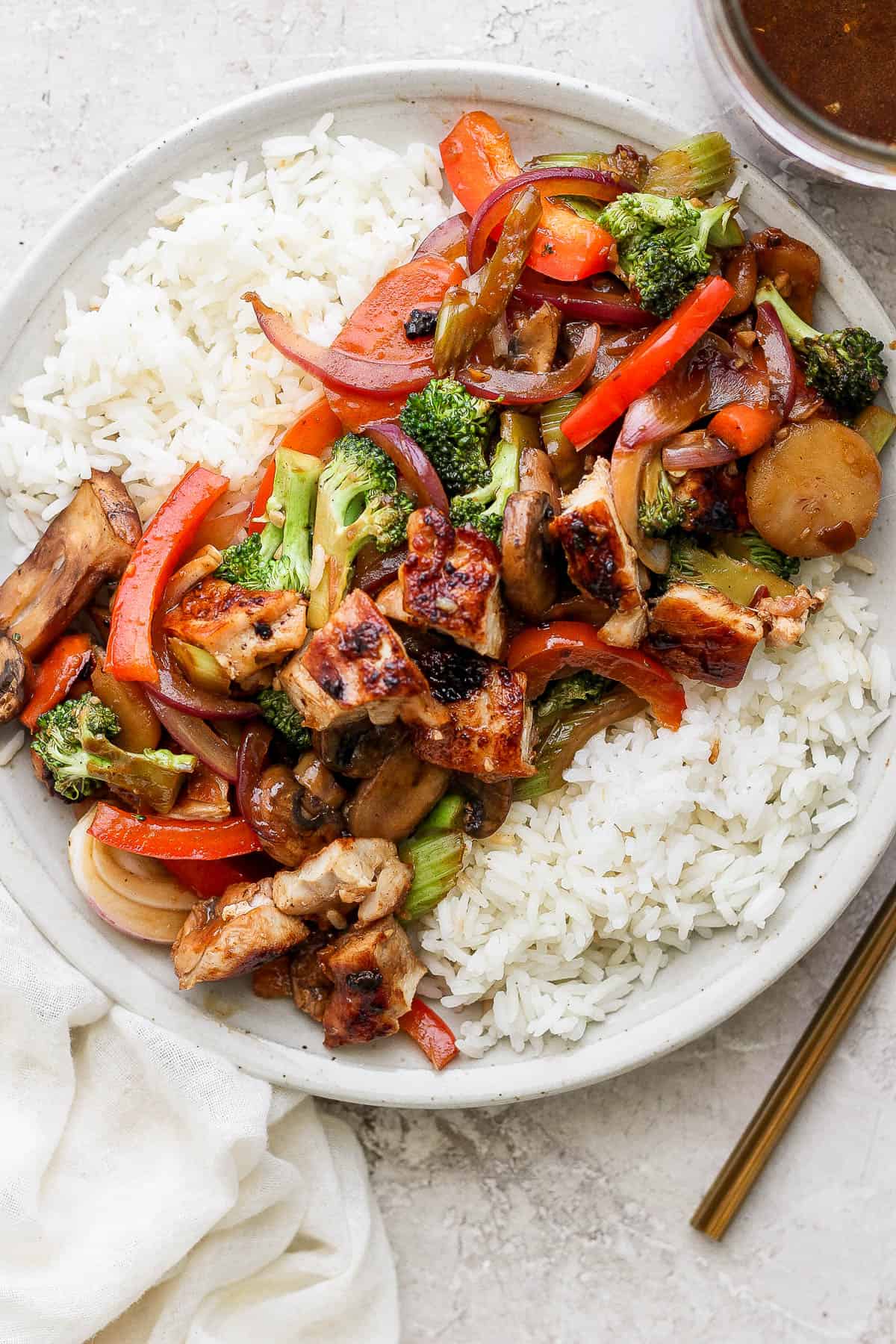 A plate with white rice and stir fried veggies and chicken on top.