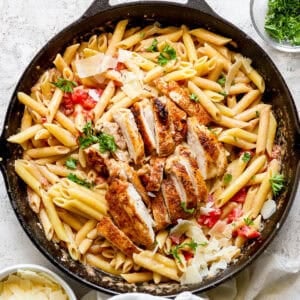 A cast iron skillet filled with cajun chicken pasta and parsley garnish.