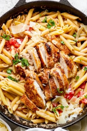 A cast iron skillet filled with cajun chicken pasta and parsley garnish.