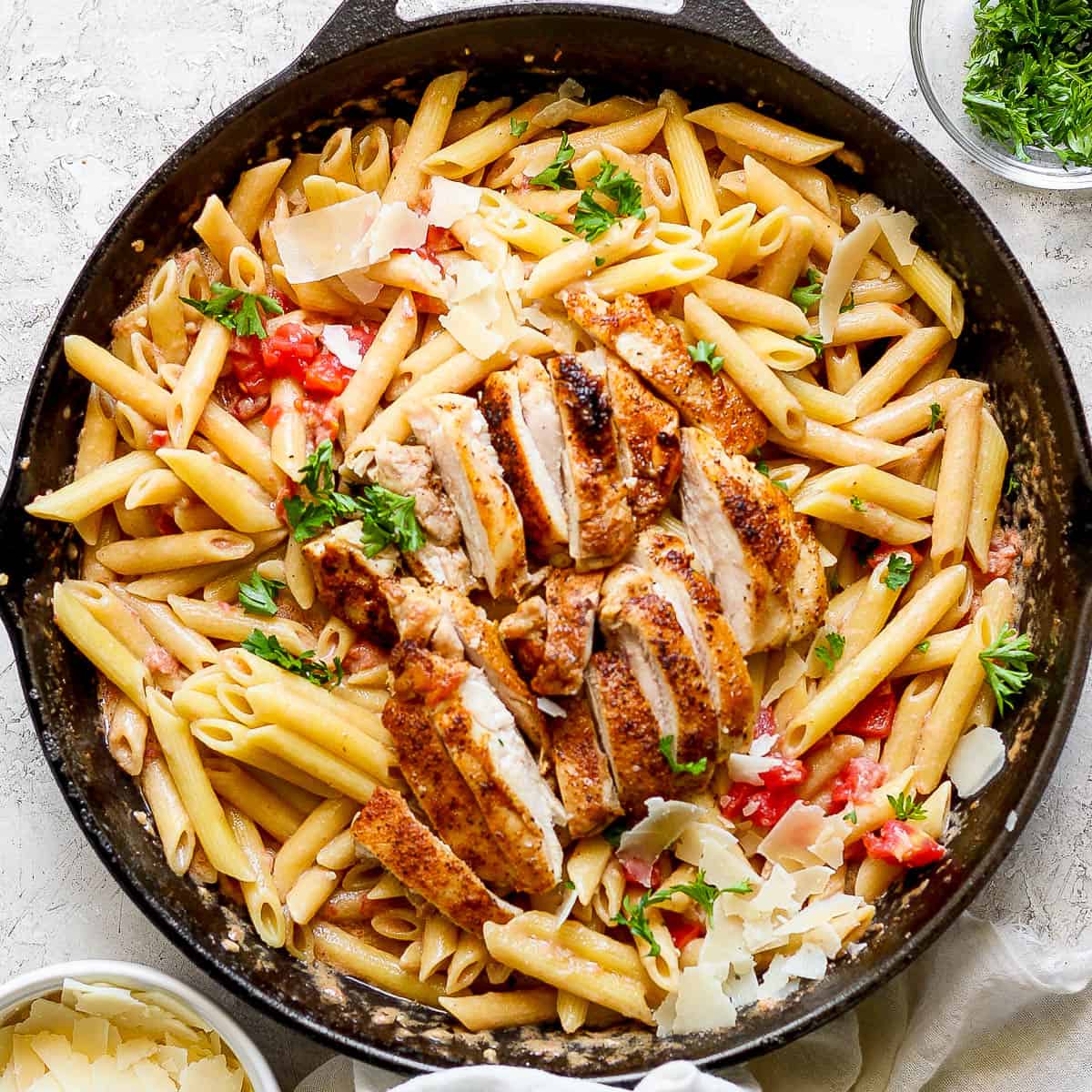 A cast iron skillet filled with cajun chicken pasta and parsley garnish.