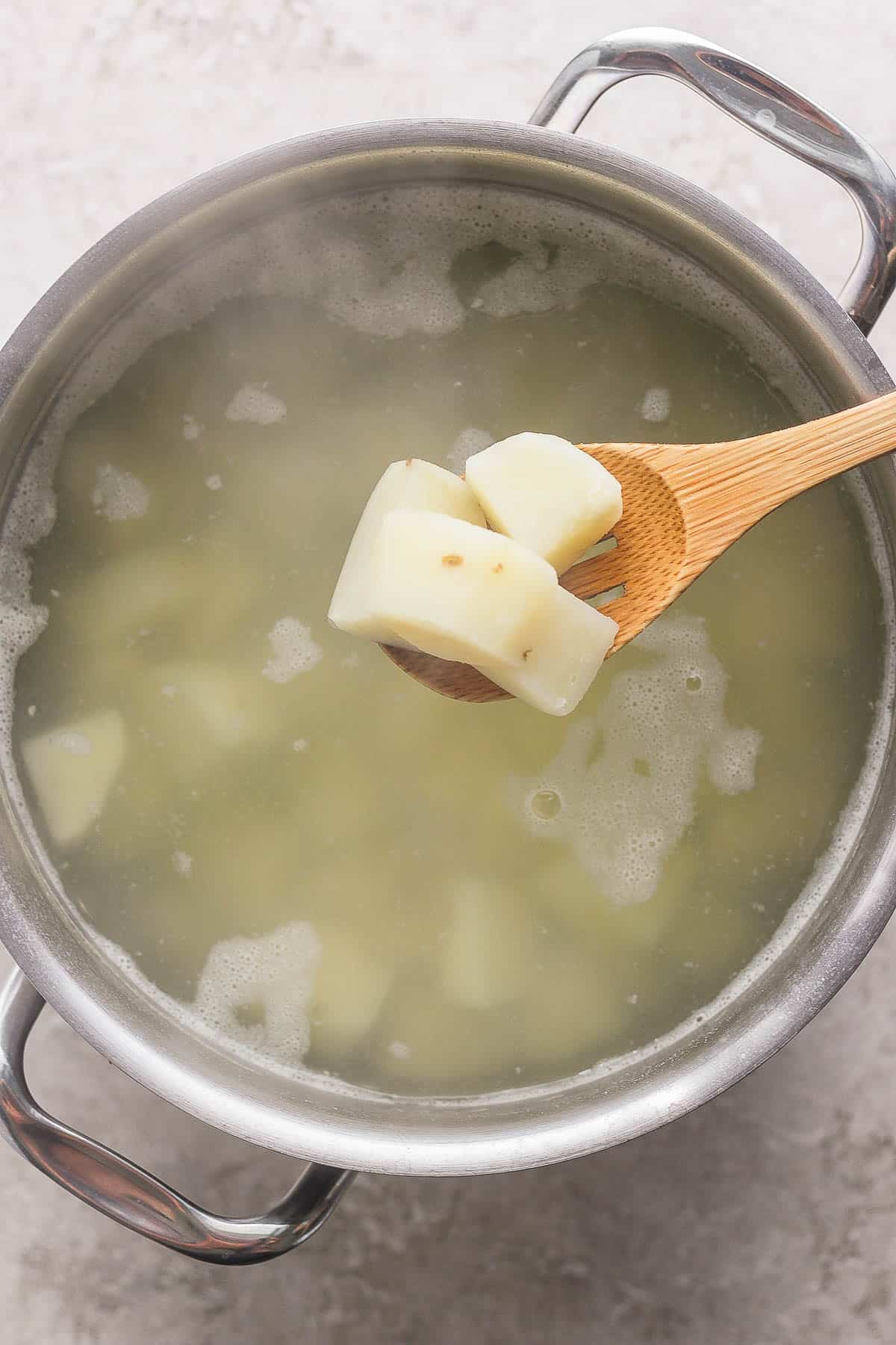 Cooked, cubed potatoes being scooped out of a pot after being boiled.