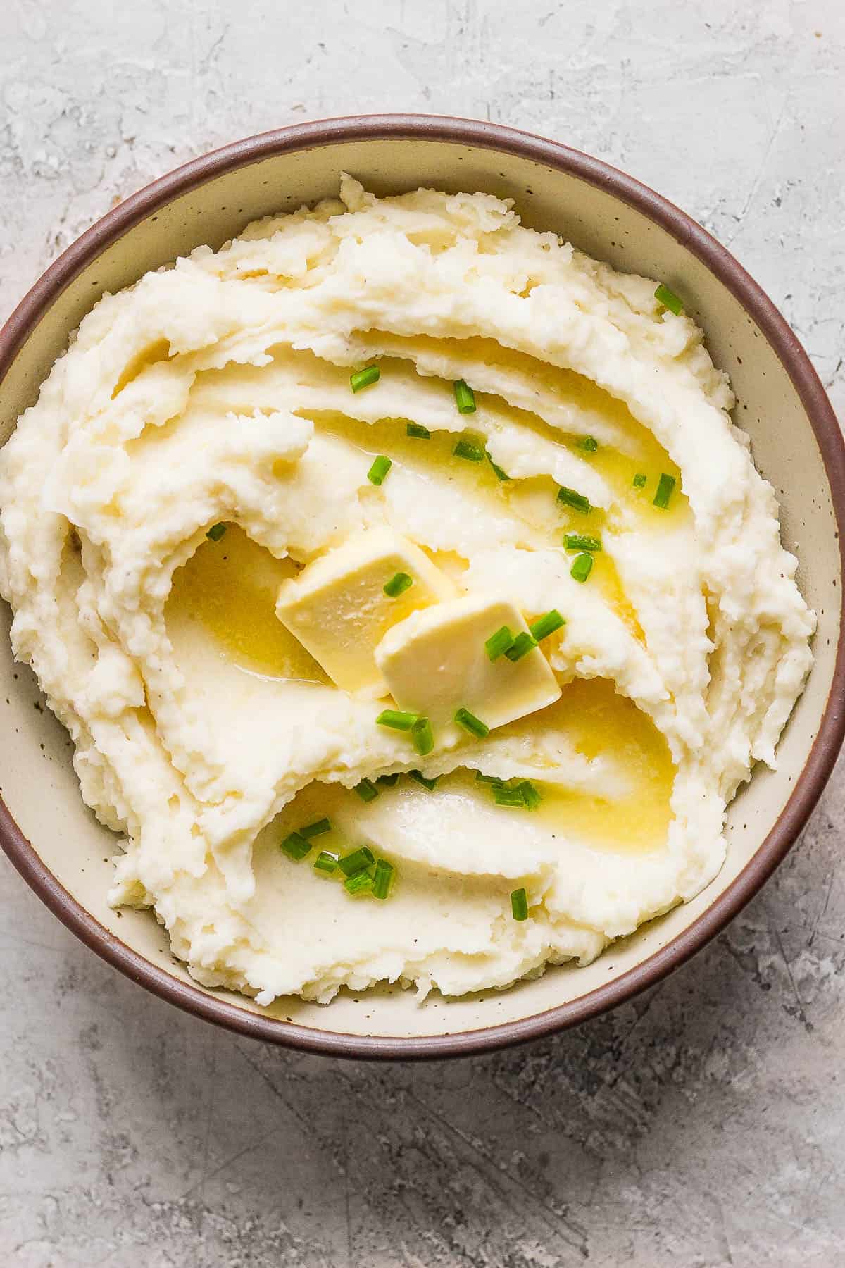 Extra creamy mashed potatoes in a bowl with butter and chives on top.