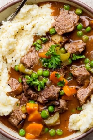 Top down shot of a bowl of dutch oven beef stew over mashed potatoes with chopped parsley for garnish.