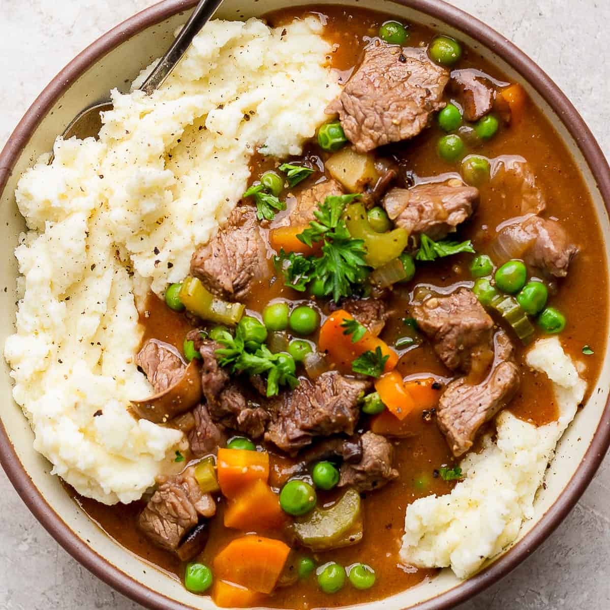 Top down shot of a bowl of dutch oven beef stew over mashed potatoes with chopped parsley for garnish.