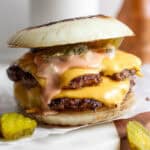 A Flying Dutchmen burger sitting on a piece of parchment with pickles next to it and burger sauce dripping down.