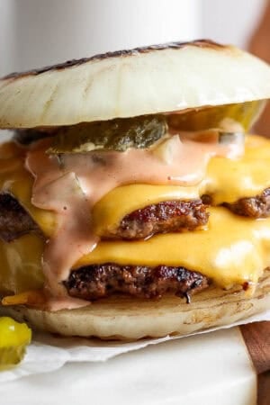 A Flying Dutchmen burger sitting on a piece of parchment with pickles next to it and burger sauce dripping down.