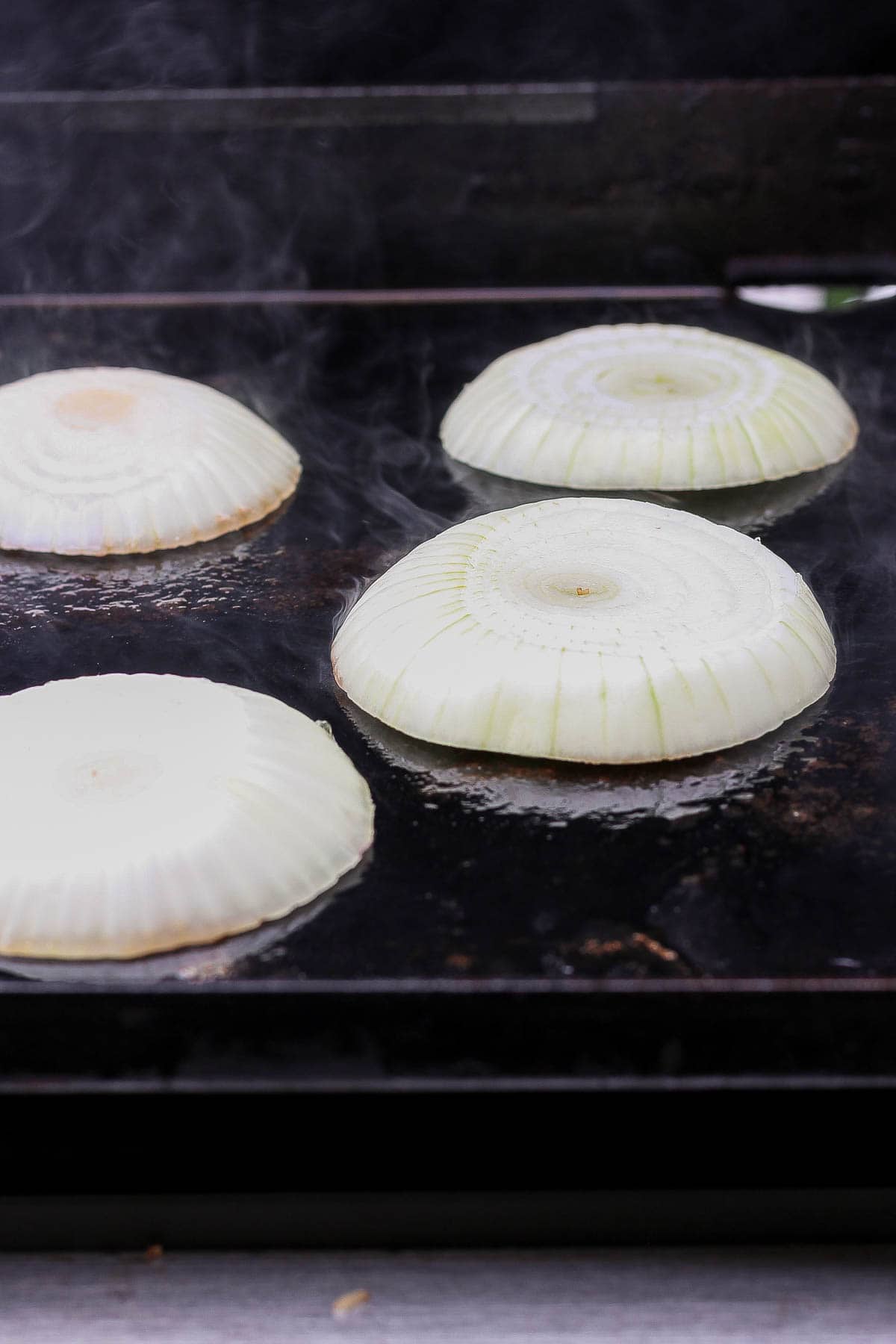 Large slices of onion on a hot blackstone grill.