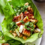 Top down shot of a grilled chicken lettuce wrap with cubed chicken, chopped cilantro, green onion and crushed peanuts.