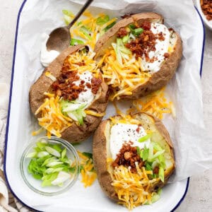 Top down shot of a platter of 3 loaded baked potatoes with sour cream, cheese, bacon and green onions on top.