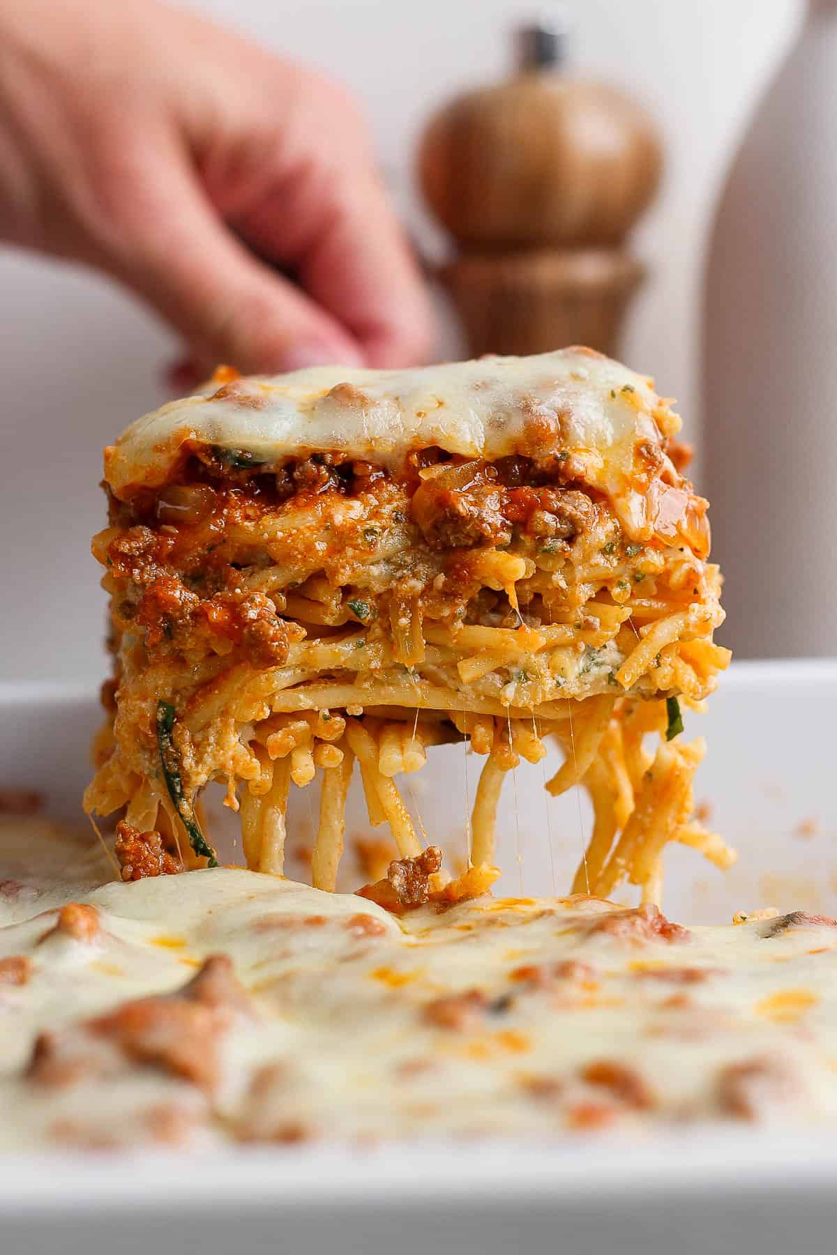 A large piece of baked spaghetti being scooped out of the baking dish.