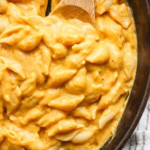 Close up shot of some pumpkin mac and cheese in a cast iron skillet with a wooden spoon.