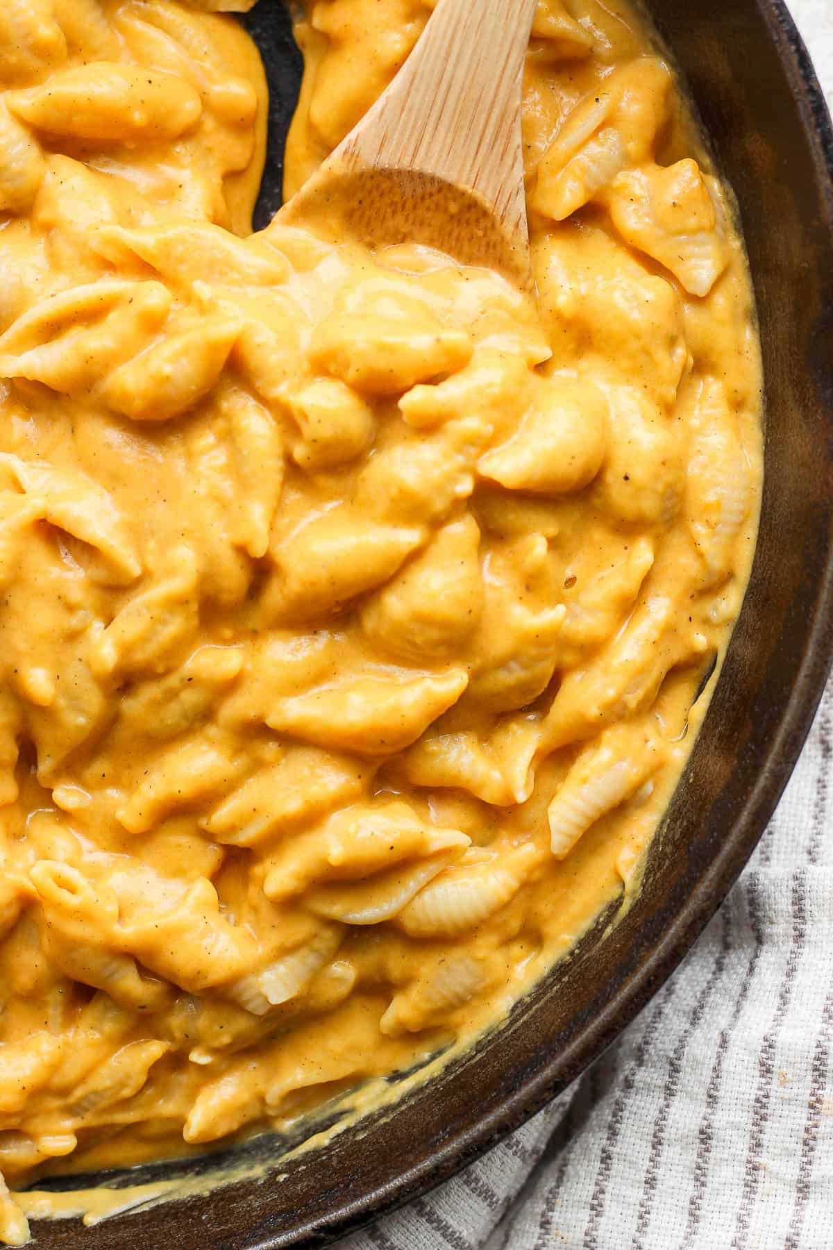 Pumpkin mac & cheese in a large skillet with a wooden spoon.