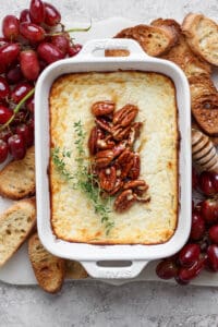 baked goat cheese dip in a casserole dish topped with pecans and honey.