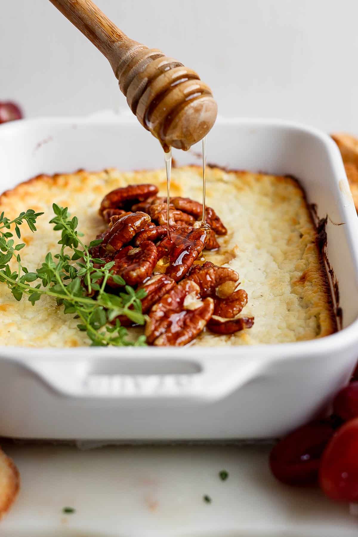 Baked goat cheese in a casserole dish topped with pecans being drizzled with honey.