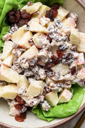 Top down shot of a bowl of homemade apple salad on top of butter lettuce with a gold spoon and fork next to the bowl.