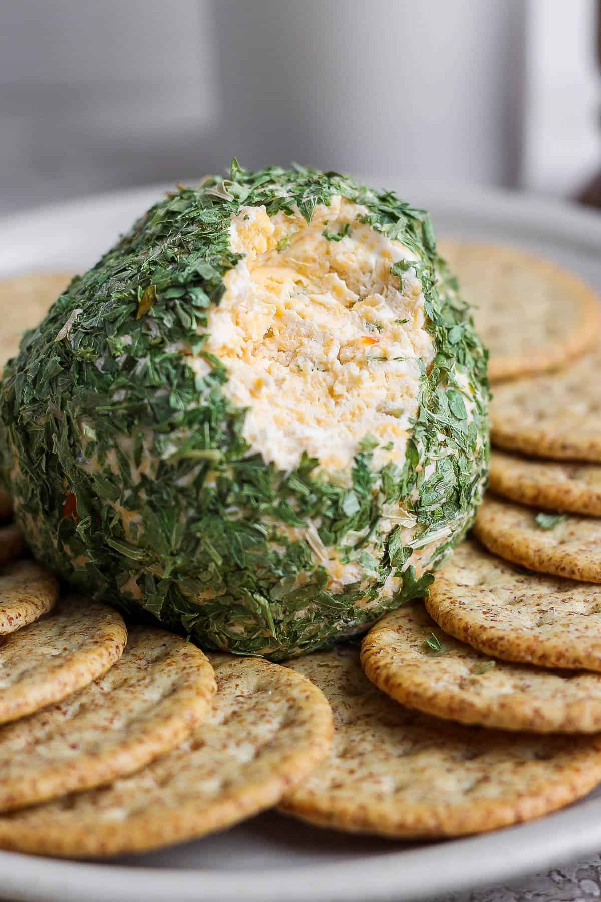 A cheese ball on a plate surrounded by crackers with a scoop taken out of it.