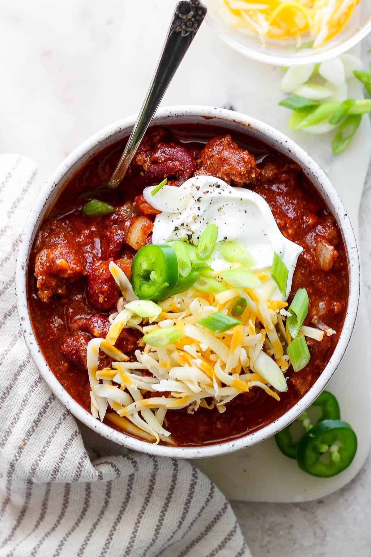 Bowl of chili topped with sour cream, jalapeno, shredded cheese, and green onion.