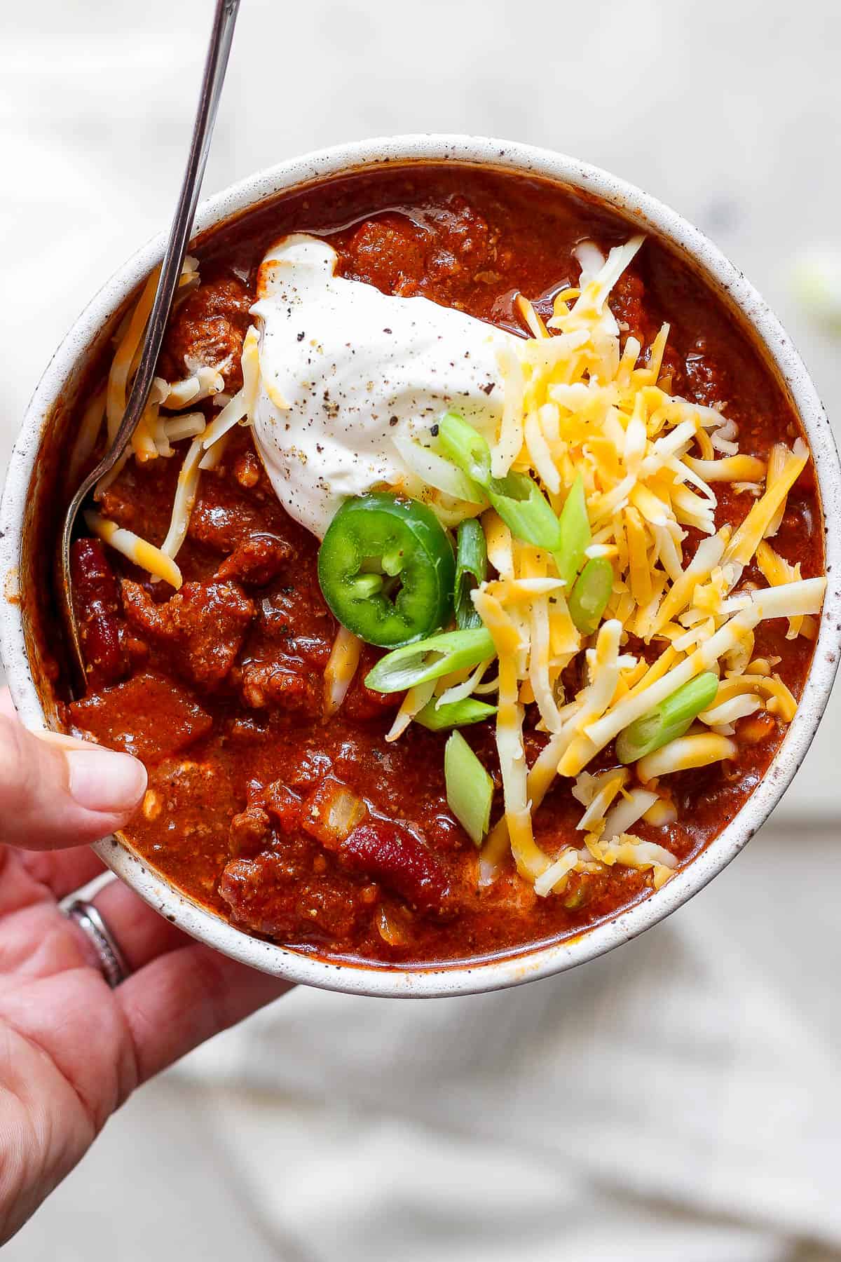 A bowl of smoked chili topped with sour cream, jalepenos, shredded cheese, and green onions.