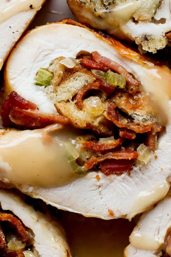 Close up top shot of a piece of stuffed turkey breast with four other pieces surrounding it with some gravy drizzled on top.