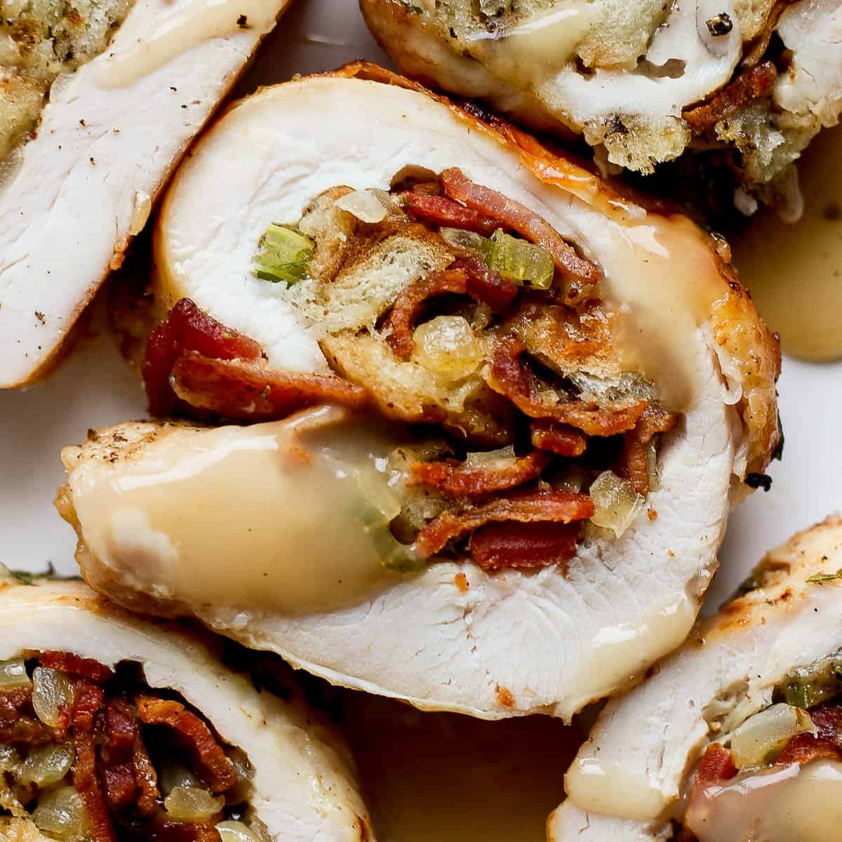 Close up top shot of a piece of stuffed turkey breast with four other pieces surrounding it with some gravy drizzled on top.