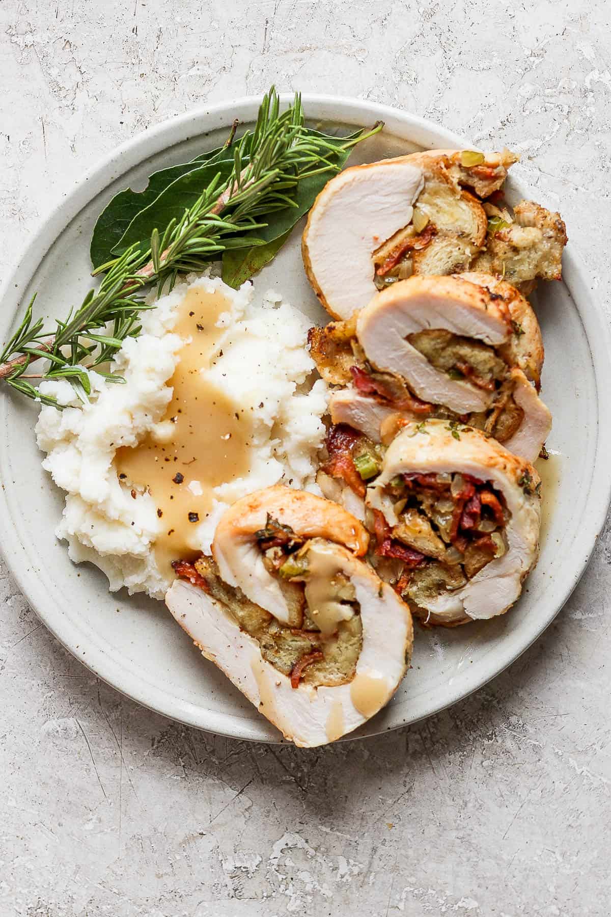 A plate with 4 slices of sliced stuffed turkey alongside mashed potatoes with gravy. 