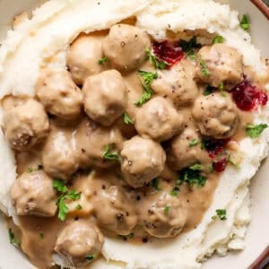 Top down shot of a big bowl of mashed potatoes topped with swedish meatballs, parsley, lingonberry jam and cracked pepper.