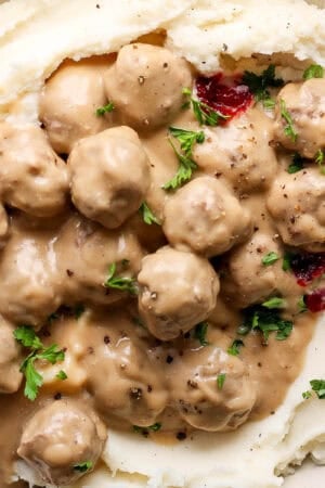 Top down shot of a big bowl of mashed potatoes topped with swedish meatballs, parsley, lingonberry jam and cracked pepper.