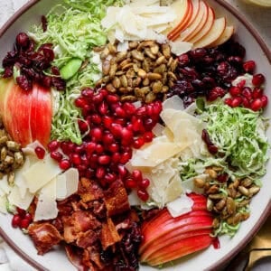 Top down shot of a big bowl filled with a brussel sprout salad with apples, pomegranate seeds, parmesan cheese, bacon, pepitas and shaved brussel sprouts.