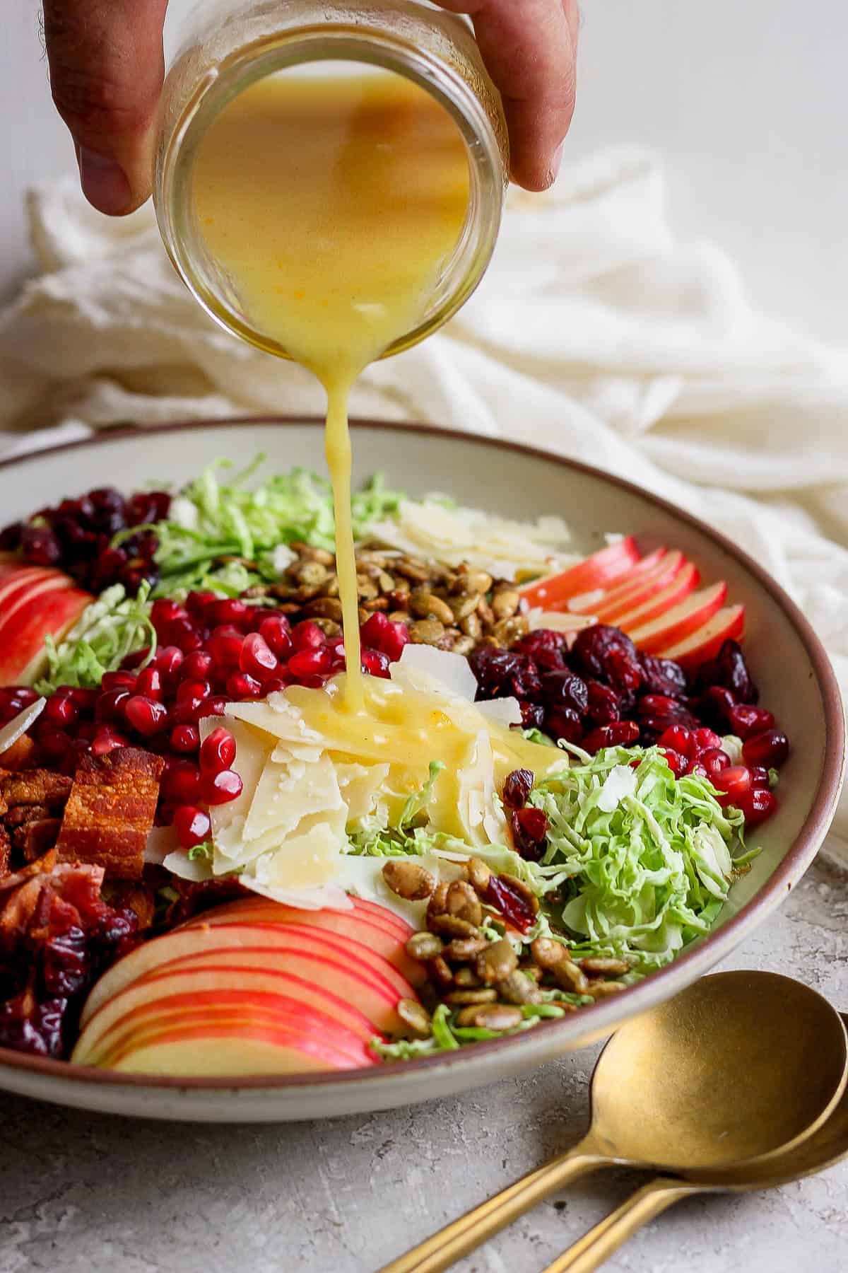 A hand pouring dressing over a large bowl of brussel sprout salad.