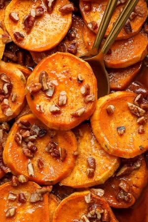 Top down shot of a close-up of candied yams in a casserole pan with chopped pecans and two spoons sticking out.