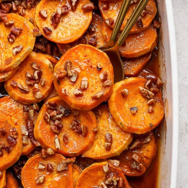 Top down shot of a close-up of candied yams in a casserole pan with chopped pecans and two spoons sticking out.