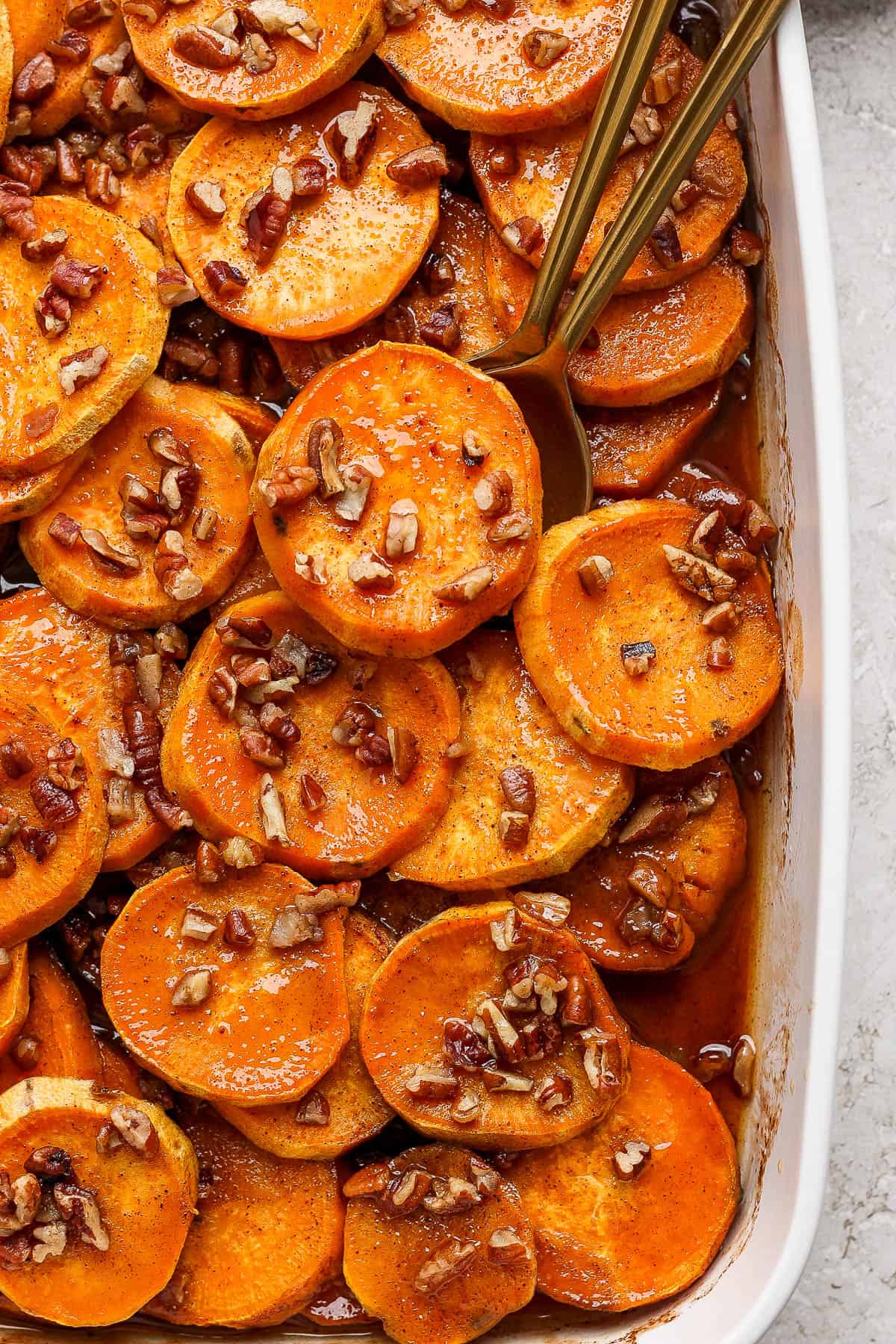 Candied yams sprinkled with chopped pecans in a casserole dish